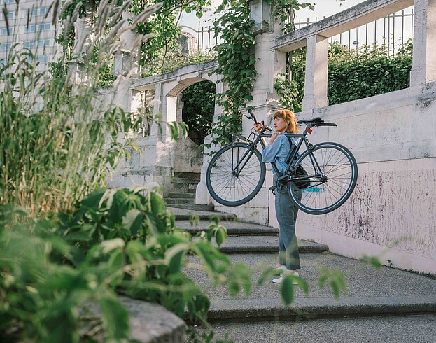 Woman carrying a bike up stairs in green surrounding