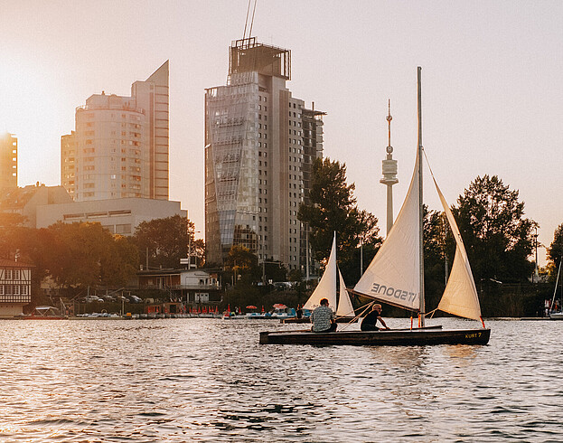 Startup Life Vienna Danube River A boat sailing on a river with modern tower blocks in the background at sunset