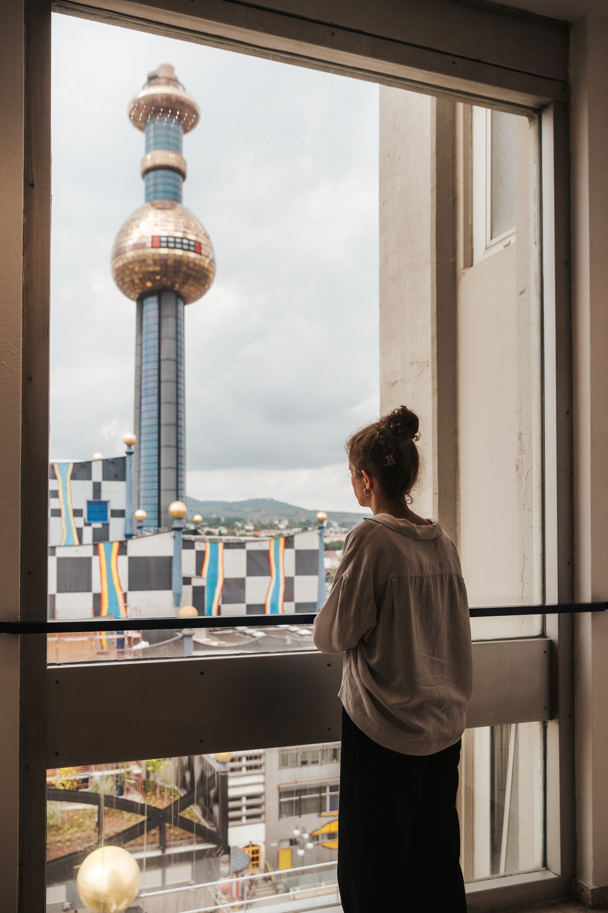Woman from the back standing by a window and looking at Spittelau in Vienna